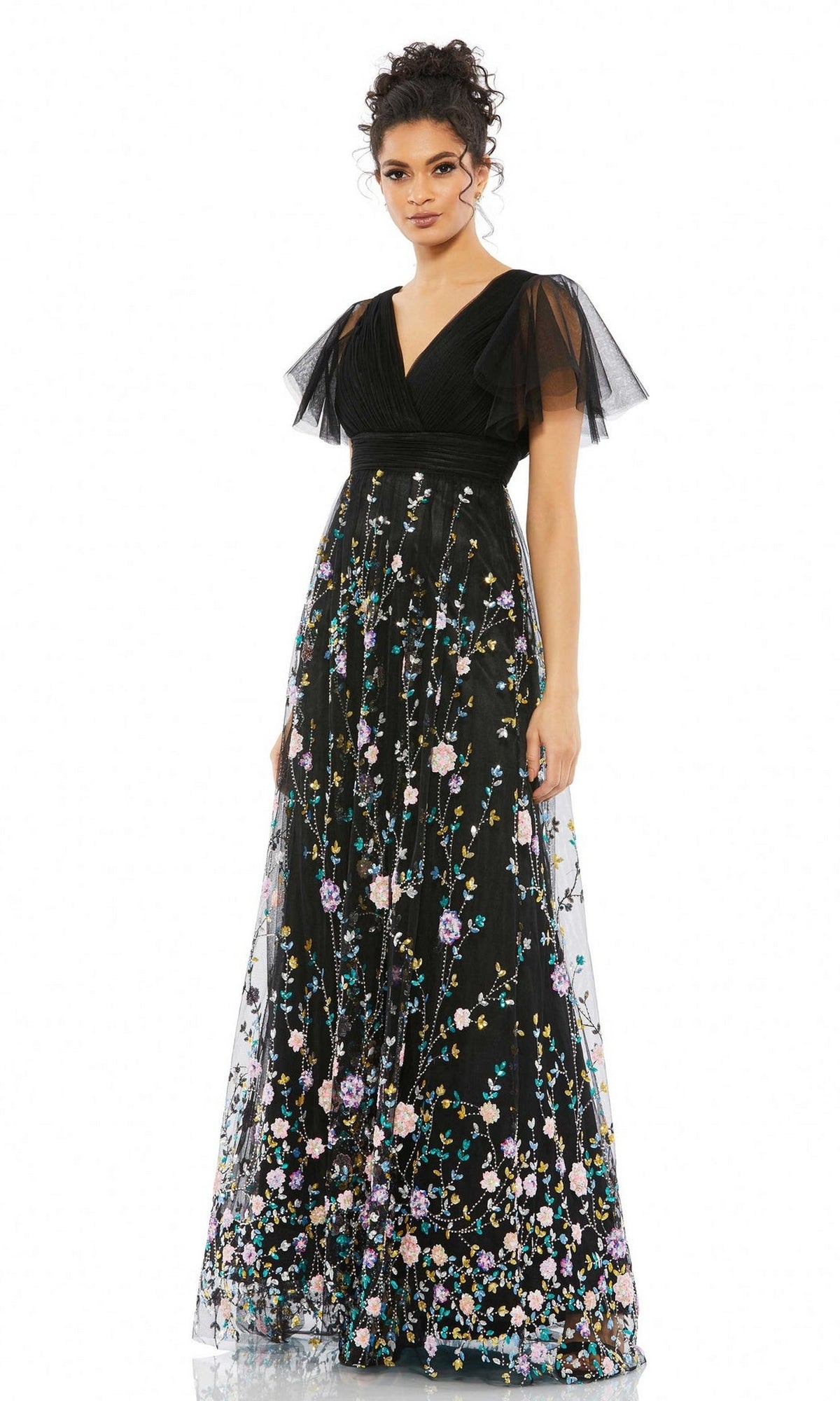 A woman wearing the Mac Duggal 67889 Black Long Floral Formal Dress with sheer flutter sleeves and colorful floral embroidery stands facing forward against a white background.
